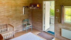 Interior d'una cabana de fusta amb una bressol, una cadira, una perxa per a abrics i una porta que dona a l'exterior.