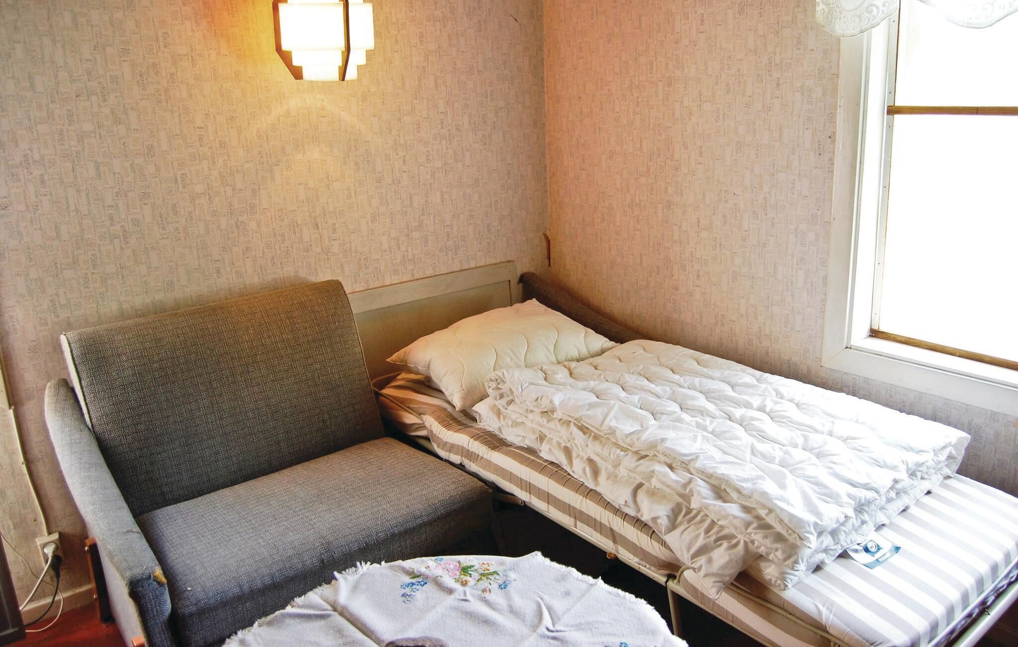 Ein kleines Zimmer mit einem Einzelbett, einem grauen Sofa, einem Nachttisch und einer wandmontierten Lampe.