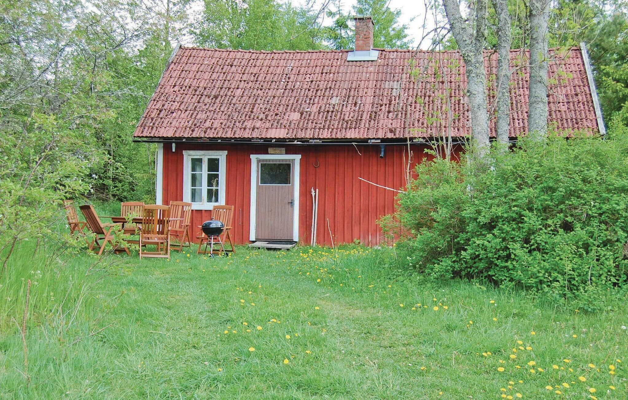 Une petite cabane en bois rouge, avec un toit en tuiles, une porte et une fenêtre. On y trouve des chaises en bois et un barbecue à l’extérieur.