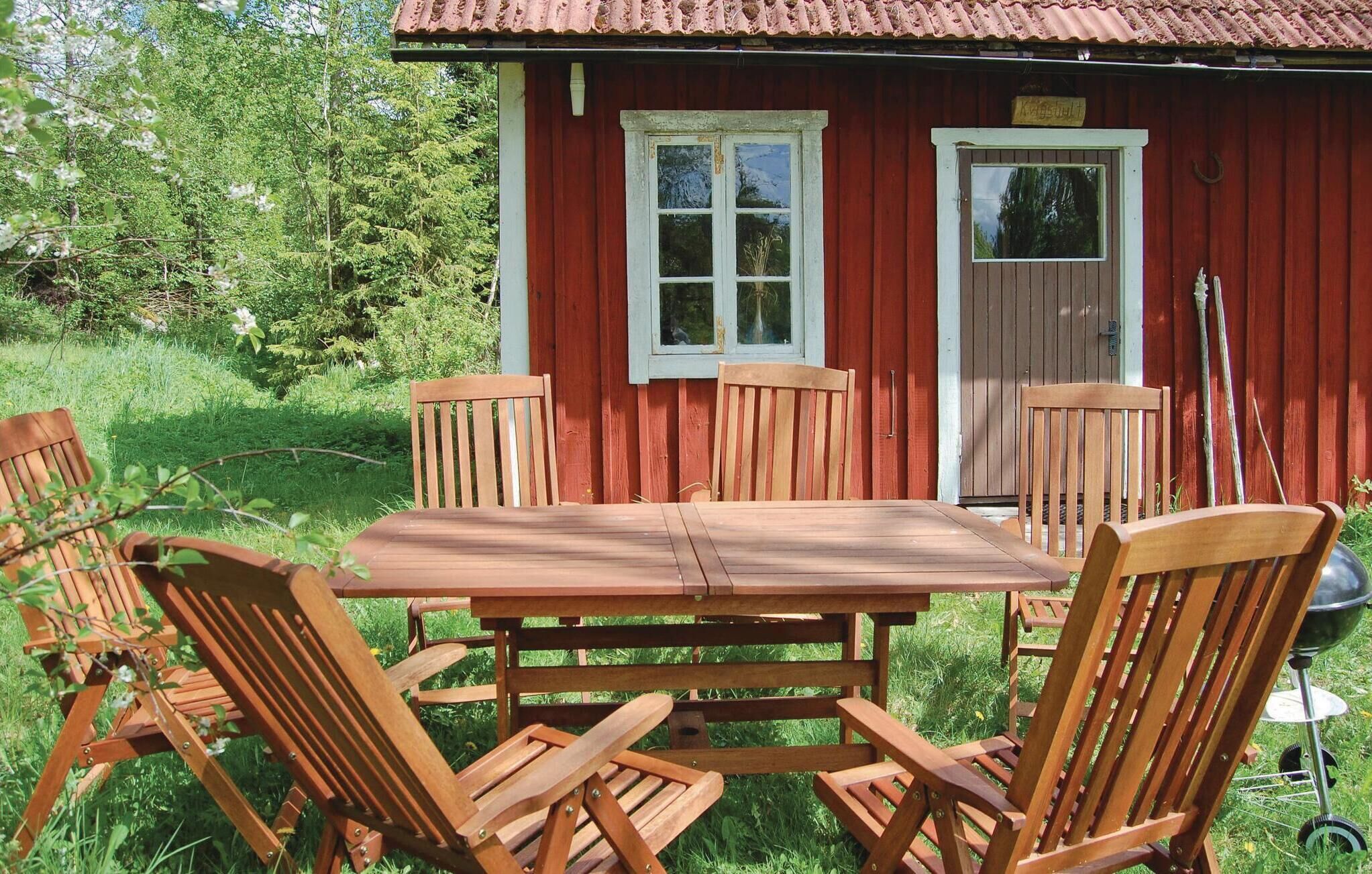 Une table et des chaises en bois sont disposées à l’extérieur, avec un bâtiment rouge en arrière-plan.
