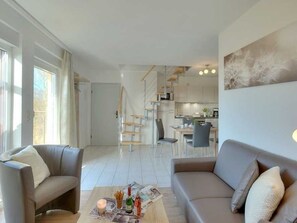 En moderne stue med sofa, sofabord og et spiseområde i baggrunden.