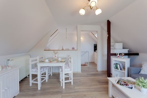 A cozy, well-lit room with a dining table, chairs, a bookshelf, and a staircase leading to another level.