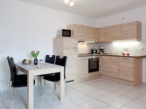 Une cuisine moderne avec des meubles de couleur bois clair, une table à manger avec des chaises, un four à micro-ondes, une machine à café et un four traditionnel.