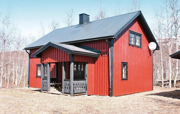 A red wooden house with a black roof, a porch, and a chimney.