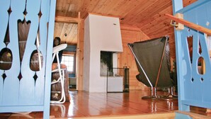Une pièce avec un plafond en bois, un réfrigérateur blanc, une chaise pliante et une porte bleue ornée de motifs découpés.