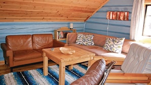 Une pièce mansardée chaleureuse avec un plafond en bois, un canapé en cuir marron, une table basse en bois et un tapis à motifs.