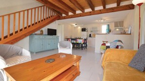 Un salon chaleureux avec un escalier en bois, un coin repas et une cuisine.