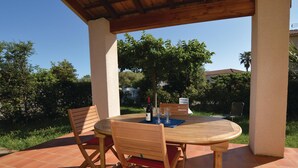 Une terrasse extérieure avec une table ronde en bois et deux chaises en bois, une bouteille de vin et deux verres à vin posés sur un tapis bleu.