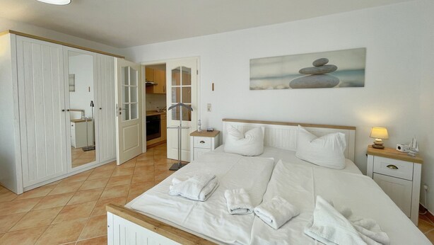 Een slaapkamer met een bed, nachtkastjes, een schilderij en een badkamer die door een open deur zichtbaar is.