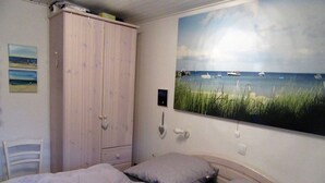 Ein Schlafzimmer mit einem Bett, zwei Kissen, einem Holzschrank und einem Wandbild mit Booten auf dem Wasser.