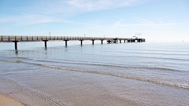 Eine Pier, die sich in ruhiges Wasser erstreckt, mit blauem Himmel darüber.