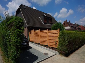 A residential house with a sloped roof, a wooden fence, and a car parked in the driveway.
