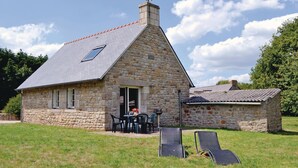 A stone house with a sloped roof and a chimney, a patio with outdoor furniture, and a grassy yard. - Amazing home in Tregunc with WiFi (Tregunc)