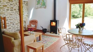 A cozy living room with a stone wall, a comfortable armchair, a wooden table, and a black wood stove. - Amazing home in Tregunc with WiFi (Tregunc)