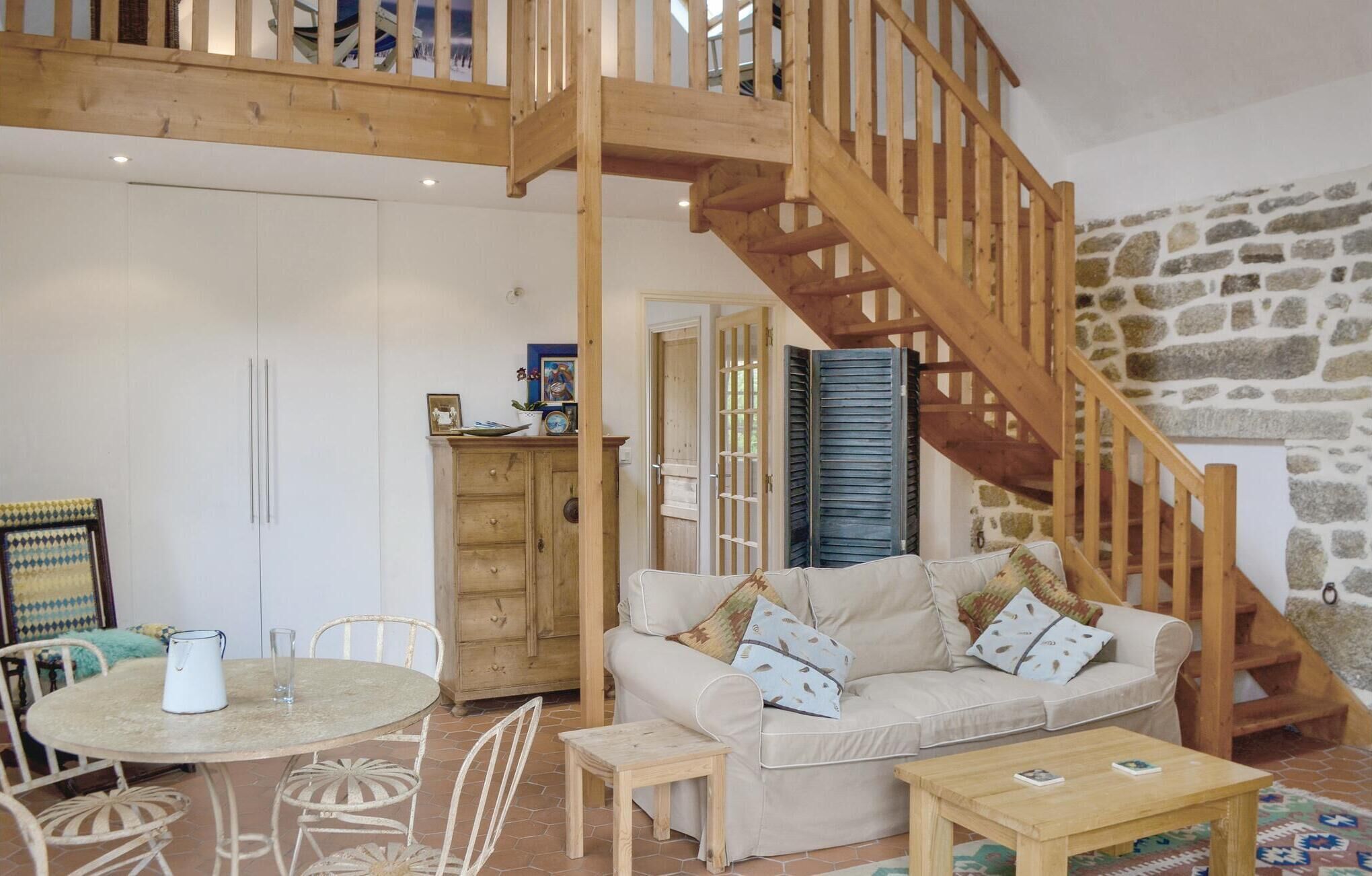 A cozy living room with a wooden staircase, a stone wall, a white sofa, a dining table with chairs, and a wooden cabinet.