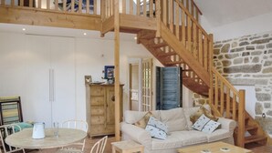 A cozy living room with a wooden staircase, a stone wall, a white sofa, a dining table with chairs, and a wooden cabinet. - Amazing home in Tregunc with WiFi (Tregunc)
