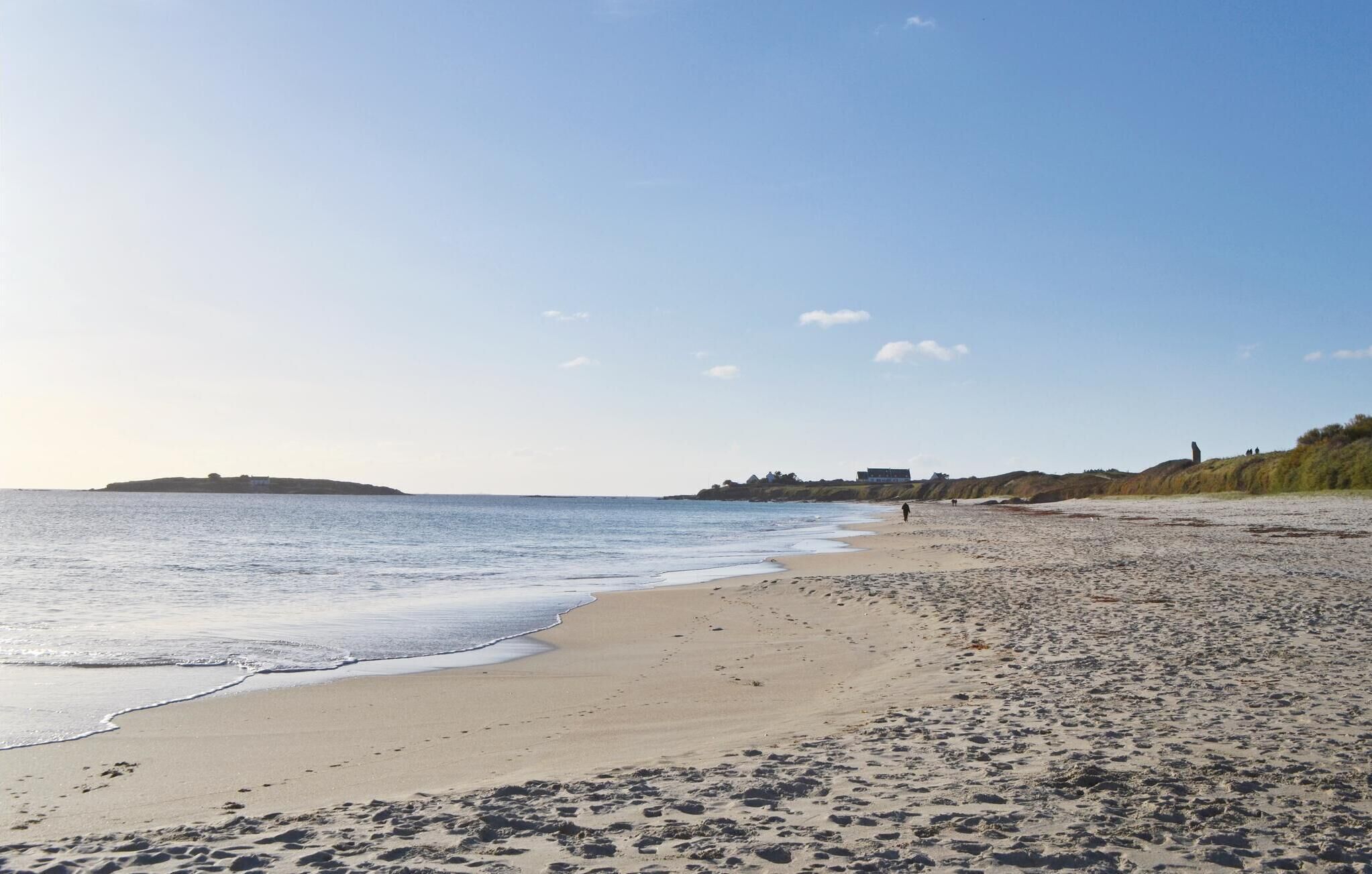 A wide sandy beach with gentle waves, a clear sky, and distant buildings on a cliff.