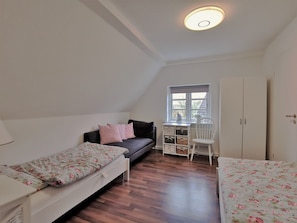 Een studentenkamer met twee eenpersoonsbedden, een bureau, een stoel en een kledingkast.