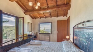 A bedroom with a large bed, a wooden ceiling, a window with a view of the countryside, a bedside table with a lamp, and a door. - Nice apartment in Loro Ciuffenna AR (Loro Ciuffenna AR)