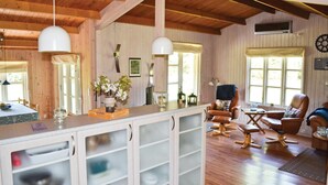Gemütliches Blockhaus-Interieur mit Holzwänden und -decke, einem Essbereich mit Tisch und Stühlen, einer Küchenzeile mit Schränken und einer Sitzecke mit Ledersesseln.