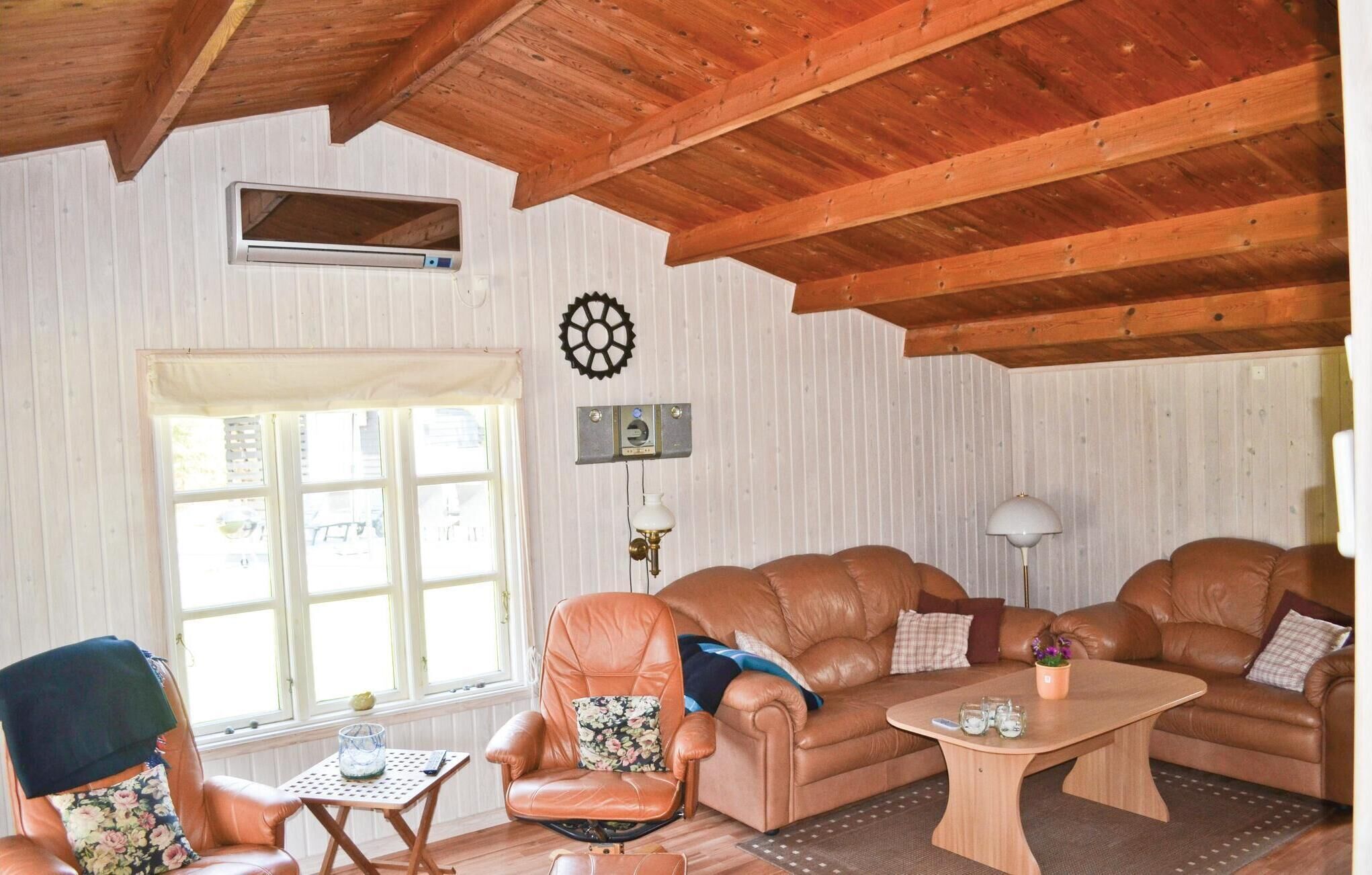 Un salon chaleureux avec un plafond en bois, un ensemble de canapés, une petite table et une fenêtre équipée de stores.