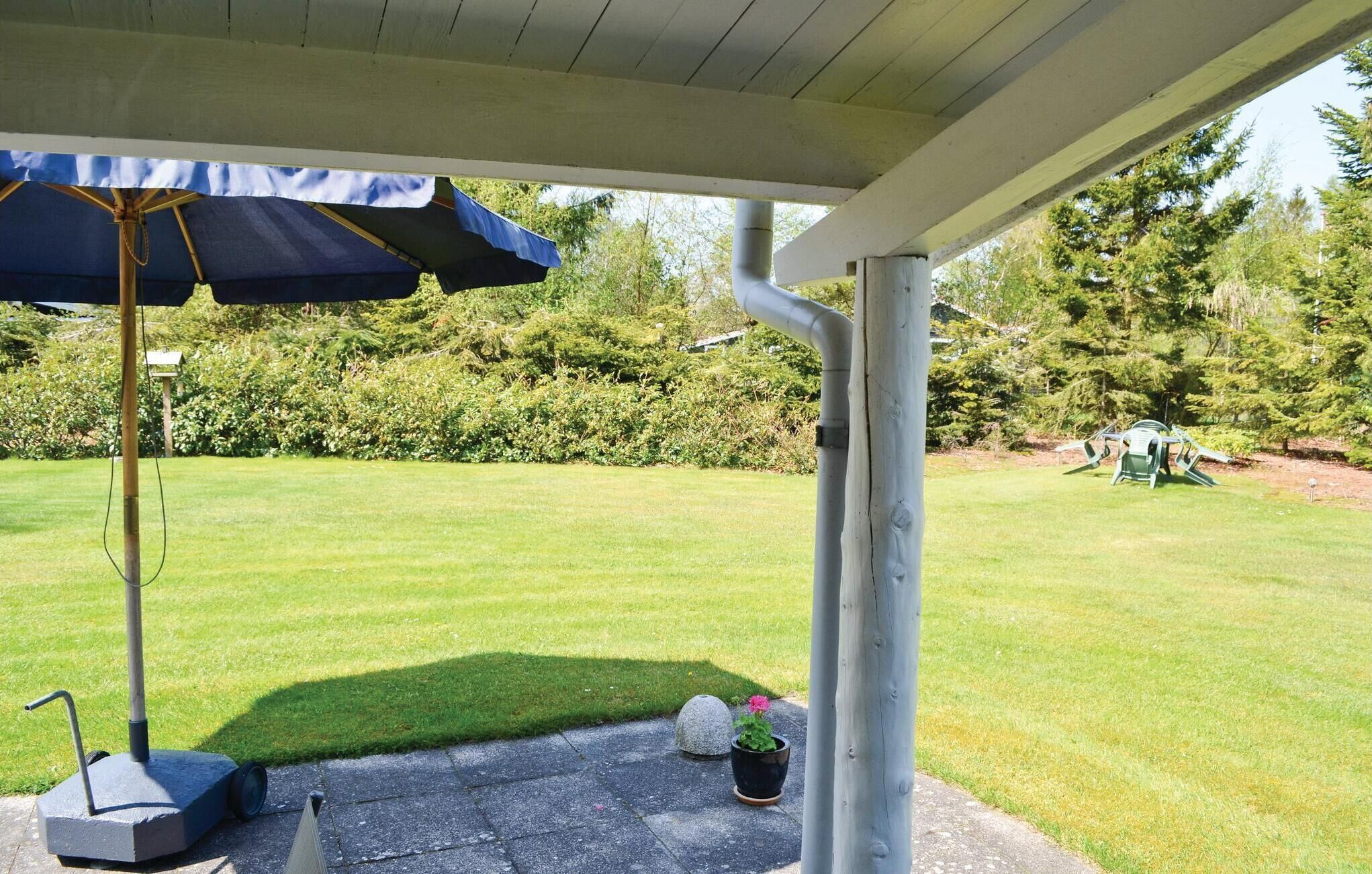 A covered patio area with a lawn, a blue umbrella, and outdoor furniture.