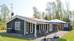Ein zweistöckiges Haus mit überdachter Terrasse und einem kleinen Nebengebäude.
