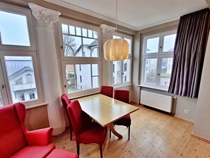 Una habitación con una mesa de madera, sillas rojas, ventanas grandes y una lámpara colgante.