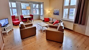 Un salon spacieux avec une grande fenêtre, un coin repas avec des chaises rouges, un canapé et un téléviseur.