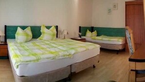 Ein Hotelzimmer mit zwei Betten, jedes mit einem grünen Kopfteil und weißer Bettwäsche. Ein Holzstuhl und ein kleiner Tisch mit einer Lampe stehen bereit.