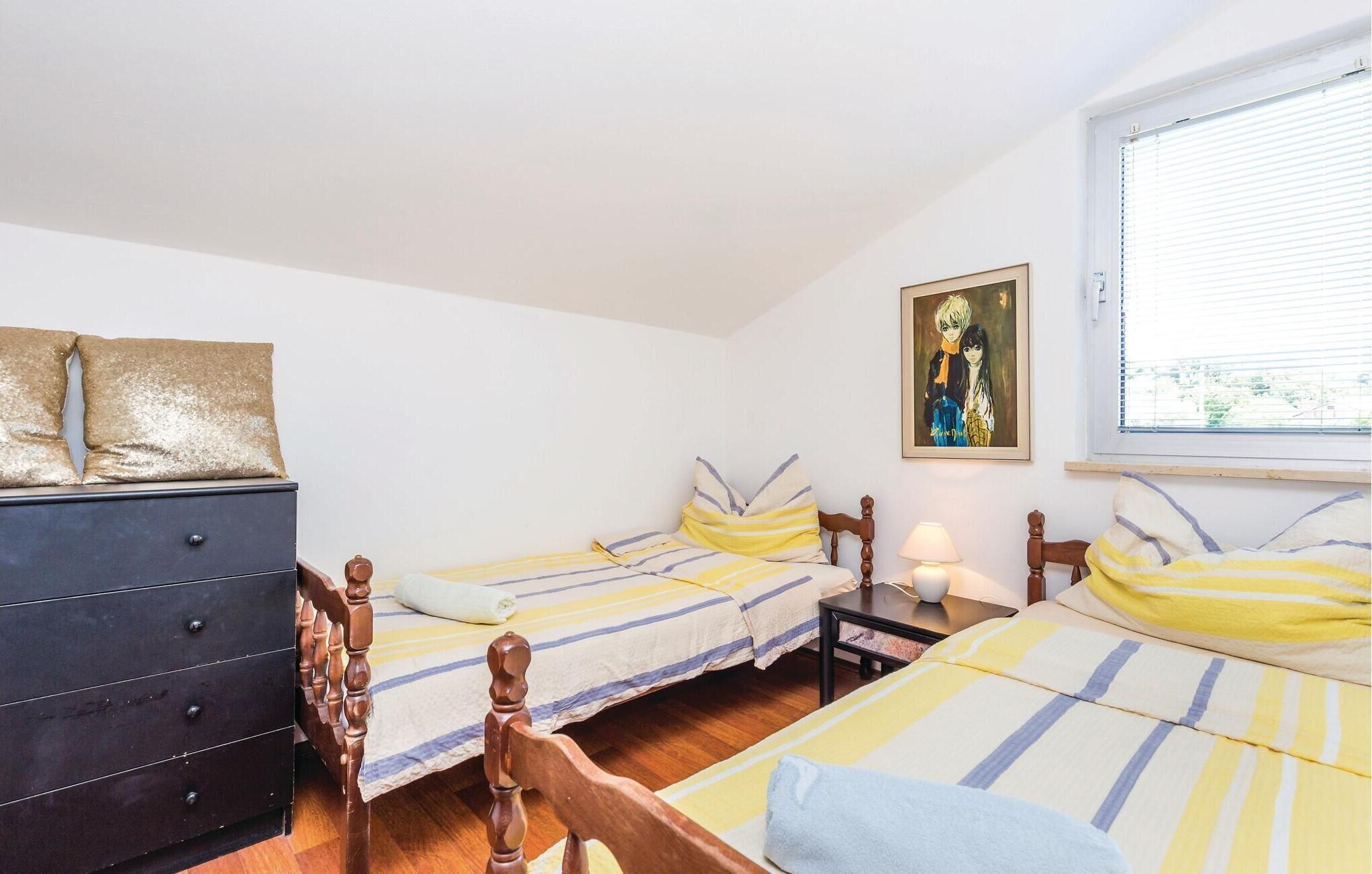 Ein Schlafzimmer mit zwei Einzelbetten, einem Schminktisch, einem Nachttisch mit Lampe und einem Fenster mit Jalousien.
