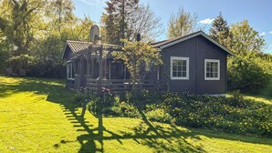 A log cabin with a porch and a satellite dish, surrounded by a well-maintained lawn and flowering plants. - 2 bedroom cozy home in Augustenborg (Augustenborg)