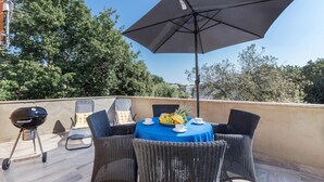 A round table with wicker chairs and a blue tablecloth, surrounded by a large black umbrella.