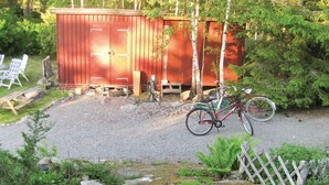 A gravel driveway leading to a red wooden shed with two doors, a bicycle parked in front, and a wooden fence surrounding the area. - Cozy home in Djurhamn with WiFi (Djurhamn)