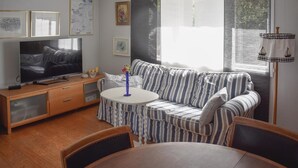 A living room with a striped sofa, a TV, a small table with a vase, and a window with curtains. - Cozy home in Djurhamn with WiFi (Djurhamn)
