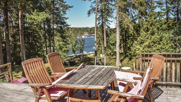 A wooden deck with a table and chairs, overlooking a lake with boats and surrounded by trees. - Cozy home in Djurhamn with WiFi (Djurhamn)