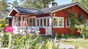 A red wooden house with a porch, a bicycle, and a garden with flowers and plants. - Cozy home in Djurhamn with WiFi (Djurhamn)