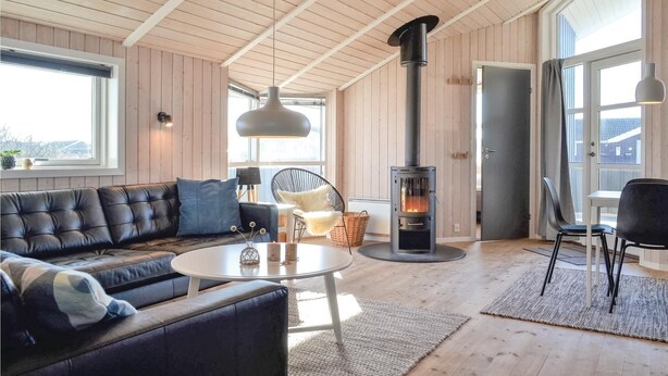 A modern living room with a black leather sofa, a round white coffee table, a large window, and a wood-burning stove. - Nice home in Hvide Sande with sauna (Hvide Sande)