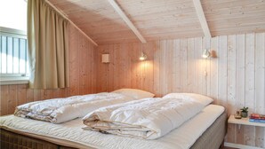 A cozy room with wooden walls and ceiling, two beds with white bedding, a window with curtains, and a small bedside table with a plant and books. - Nice home in Hvide Sande with sauna (Hvide Sande)