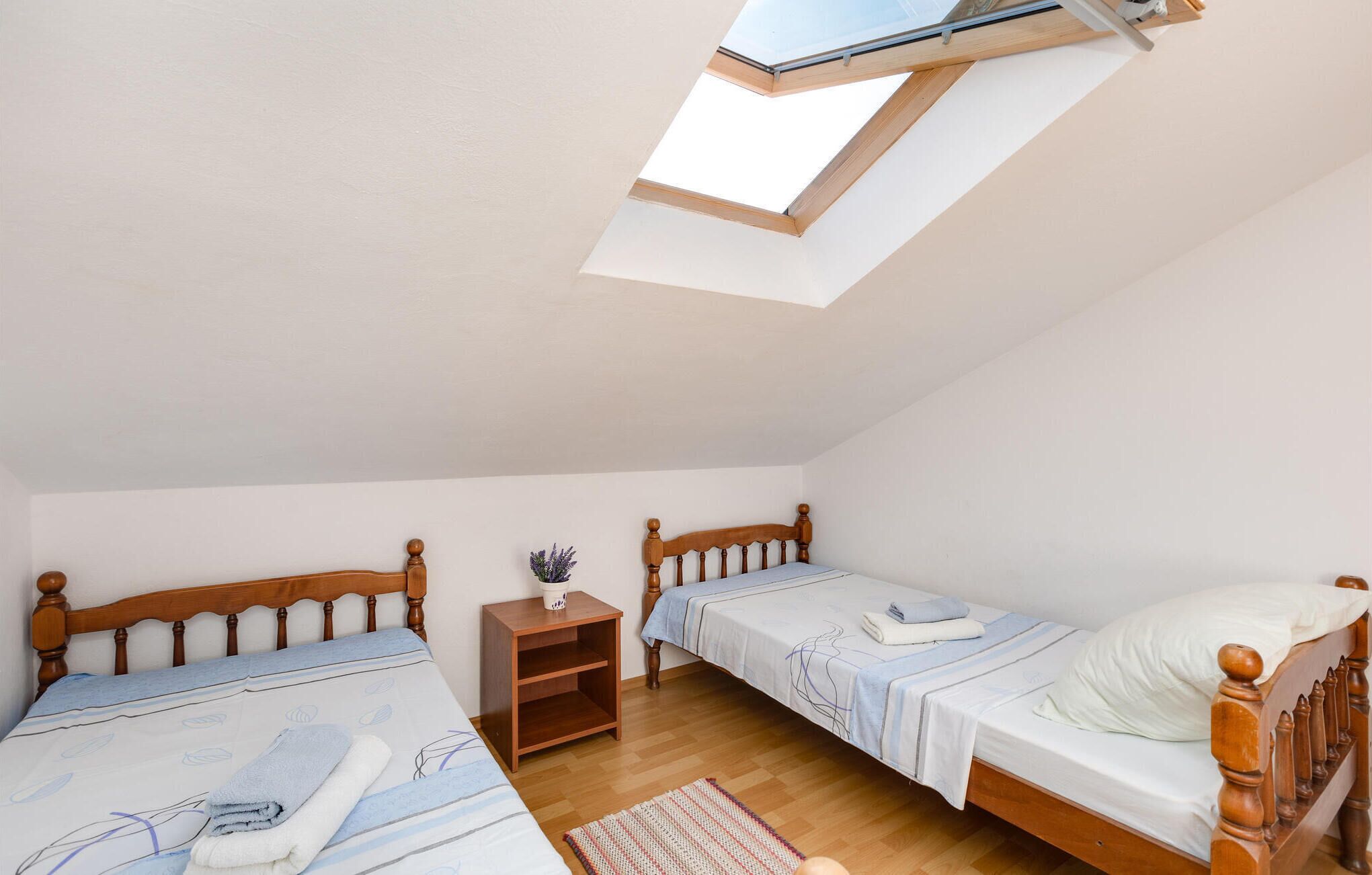 Ein kleines, helles Schlafzimmer mit zwei Holzbetten, einem Nachttisch und einem Dachfenster.