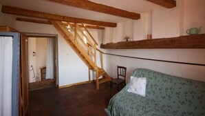 A room with a wooden staircase, a bed with a patterned bedspread, a chair, and a shelf with a teapot. - Tour Ourne Mas de Tours (Tornac)