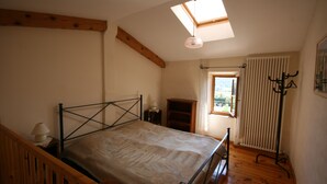 A bedroom with a bed, a skylight, a window, a radiator, and a coat rack. - Tour Ourne Mas de Tours (Tornac)