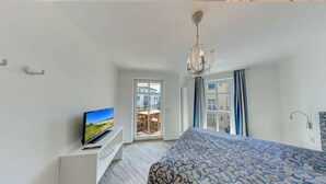 Ett modernt hotellrum med en stor säng, en tv på ett vitt stativ och utsikt över balkongen.