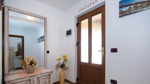 Un corridoio con una porta in legno, uno specchio e un vaso con fiori.