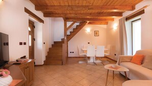 Un soggiorno con una scala in legno, un'area pranzo con sedie bianche e un divano con un cuscino arancione.