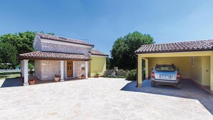 Un edificio in pietra su due piani con tetto in tegole, un carport coperto e un viale in pietra.