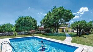 Una piscina con bordo in pietra, circondata da un prato curato e alberi.