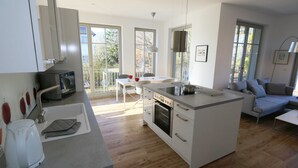 Una cucina moderna con isola centrale, zona pranzo con tavolo e sedie, e zona soggiorno con divano e lampada.