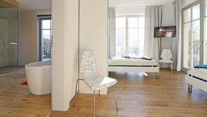 Una camera d'albergo moderna con un'ampia finestra, un letto, una televisione e un bagno.