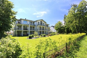 A large, two-story building with a balcony on the upper floor, surrounded by a well-maintained lawn and trees. - CSP: Villa Pauline Whg. 05 with 2 balconies - Villa Pauline Whg. 05 with 2 balconies (Göhren)